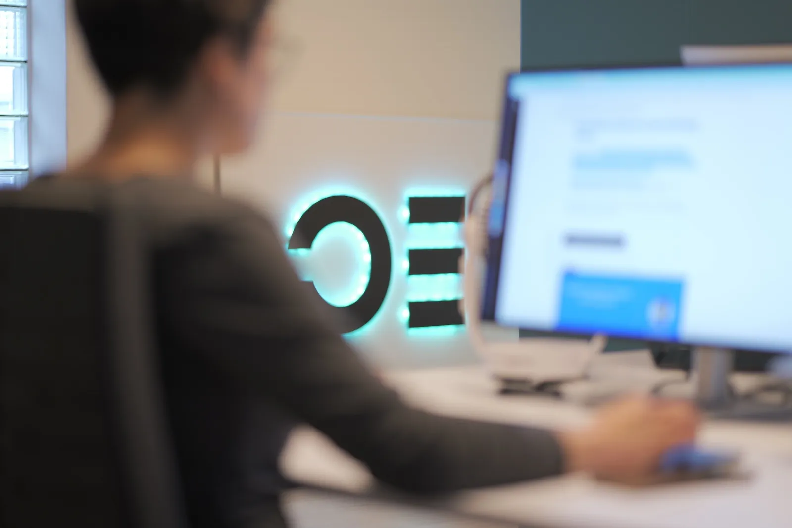 Sereina vor einem Bildschirm im Ops One Büro, Neon-Logo im Hintergrund.
