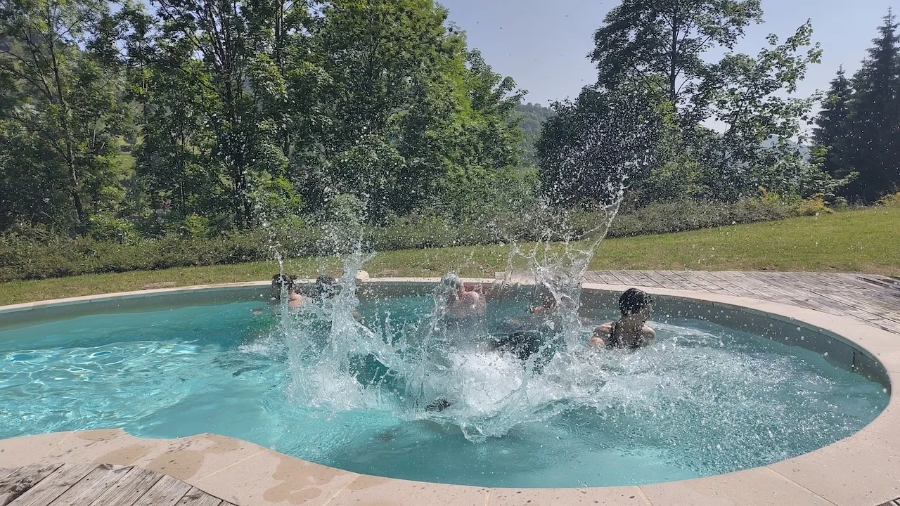1 Sekunde, nachdem Andri in den Pool gesprungen ist – Wasser spritzt auf, restlichen Teammitglieder (im Pool) drehen sich weg oder kneifen die Augen zu, Andri unter Wasser.