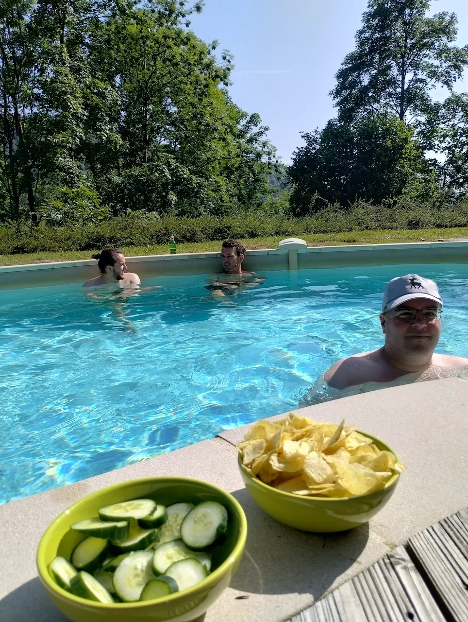 Bild vom Poolrand aus, im Vordergrund zwei Schüsseln mit Chips und Gurkenrädchen, im Hintergrund Teammitglieder am baden.