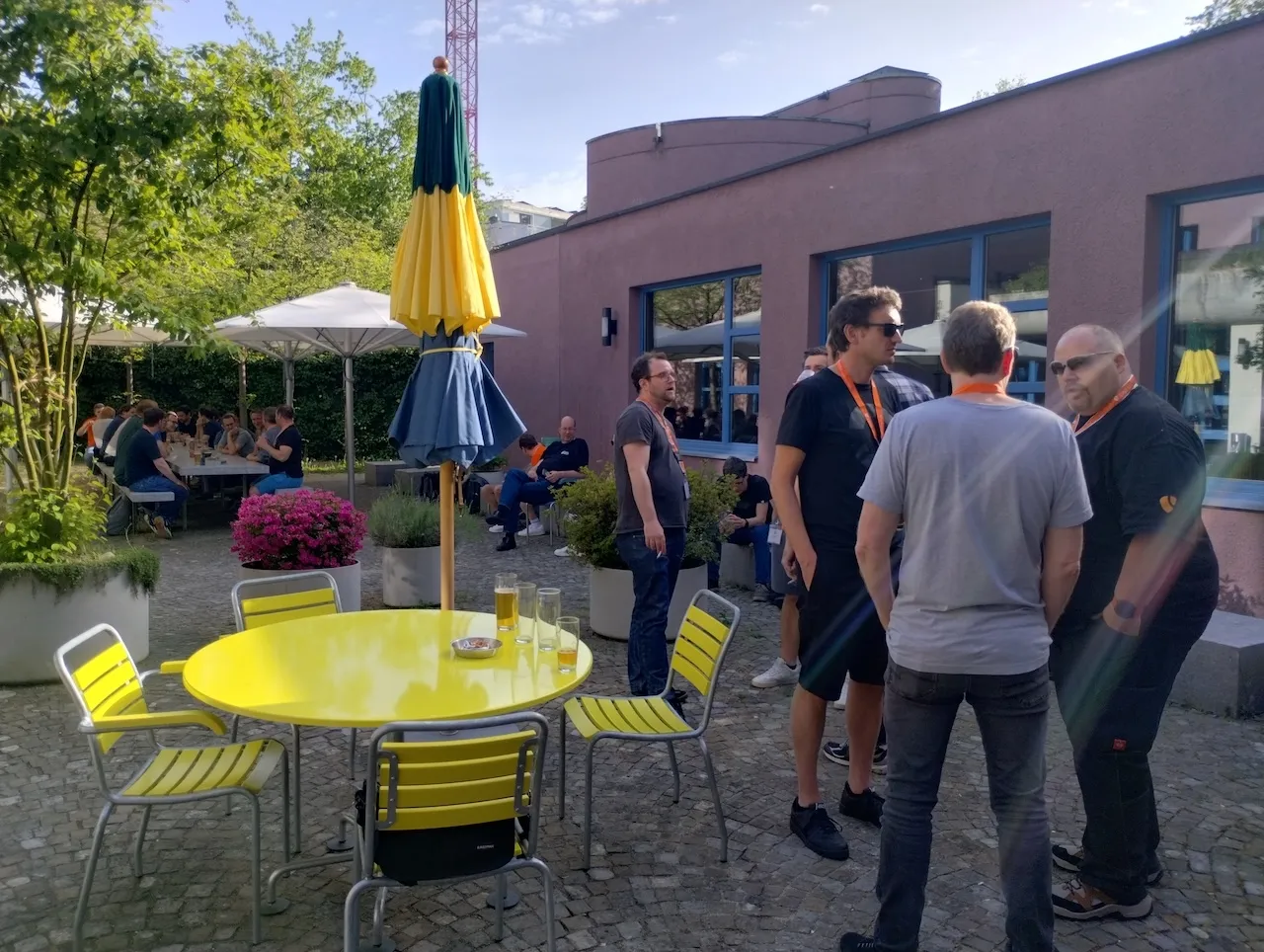 Innenhof der Jugendherberge Zürich beim Social Event, Campteilnehmende zwischen bunten Tischen und Sonnenschirmen am den Tag ausklingen lassen.