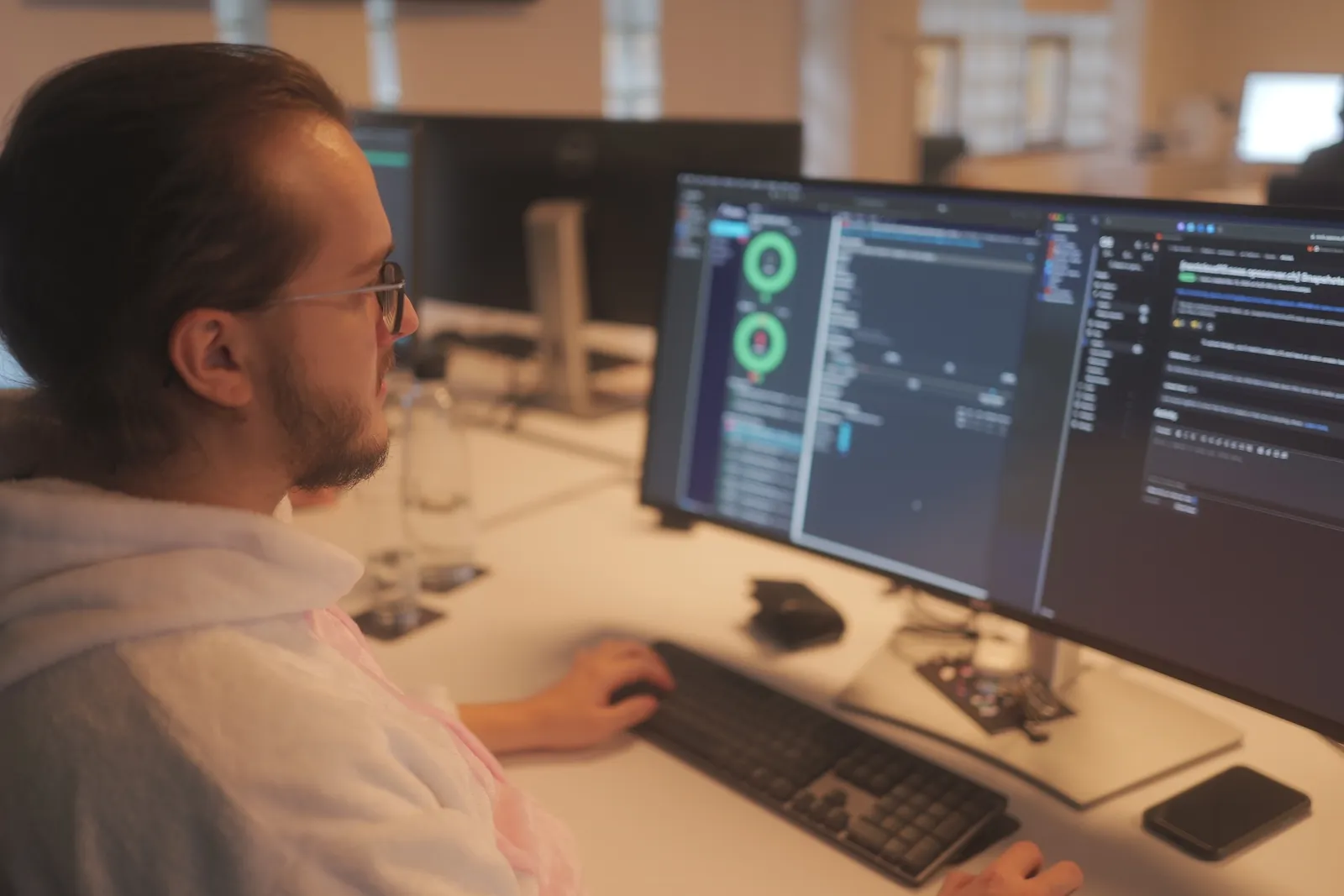 David im Ops One Büro vor seinem Bildschirm, auf dem Bildschirm offenes Test-Program, GitLab, und Terminal.